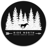Sticker in the shape of a circle with a the outline of a white horse running in front of  white evergreen trees. Below the words "RIDE NORTH - Never Knock Goods" written within an arrow 